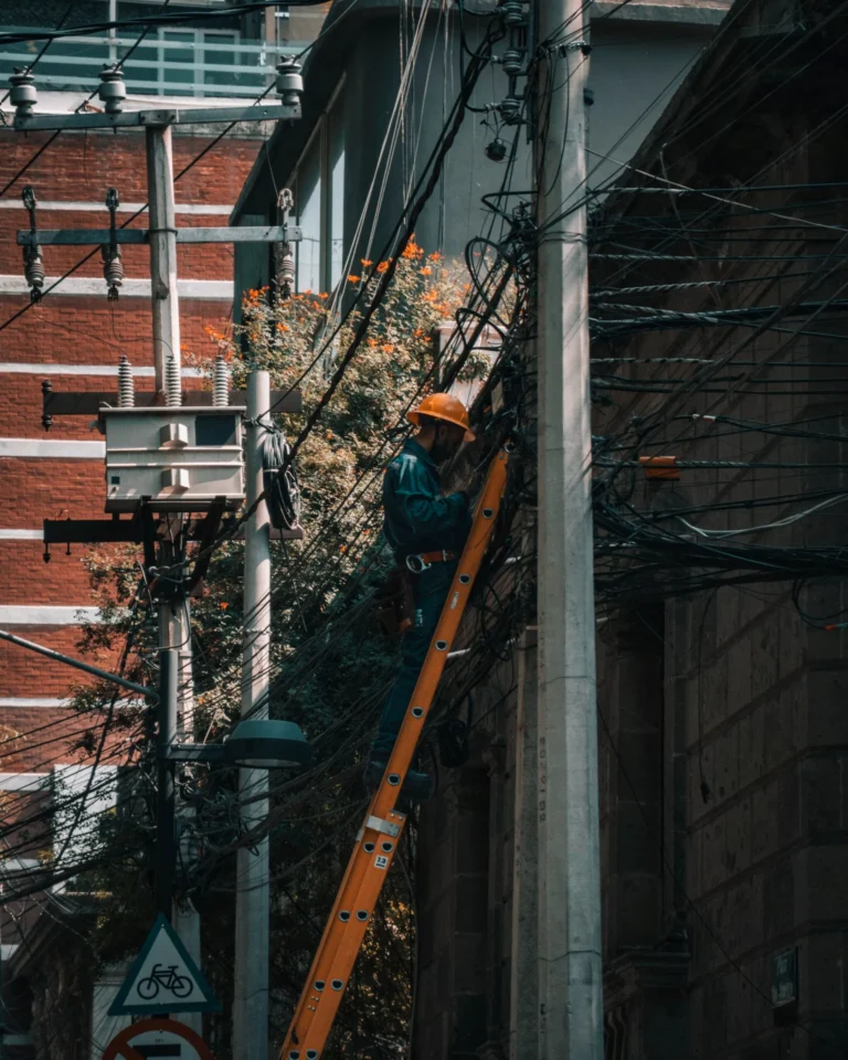 Tecnico en escalera dando mantenimiento a lineas electricas exteriores