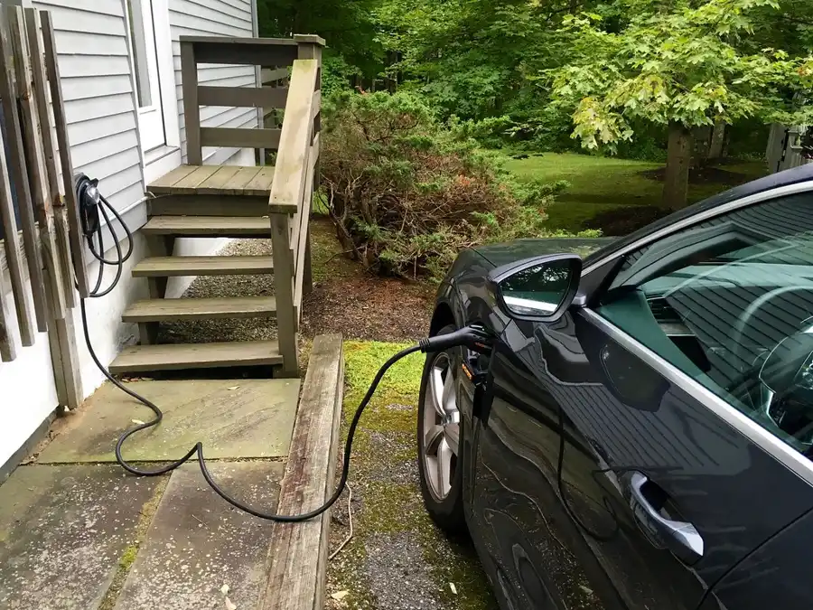 Auto eléctrico conectado a un cargador junto a la escalera de una casa