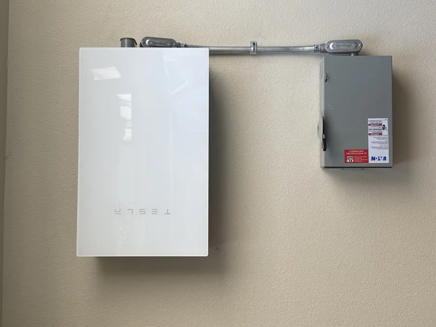 Batería solar blanca instalada en la pared junto a un interruptor de desconexión