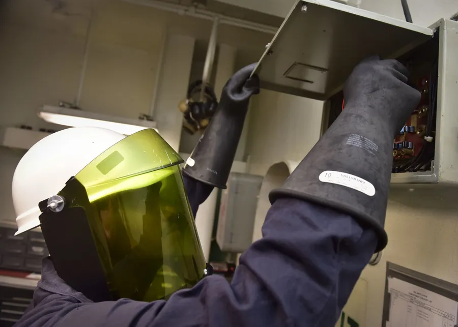 Electricista con careta y guantes dieléctricos midiendo en un tablero