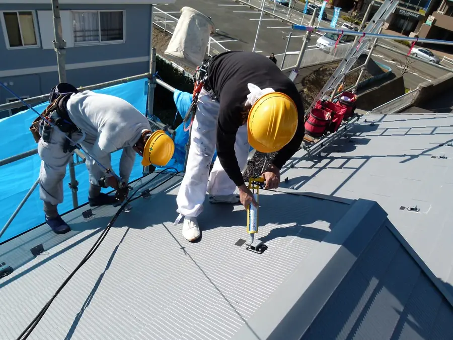 Dos instaladores con casco fijando y sellando los soportes de paneles solares en un techo