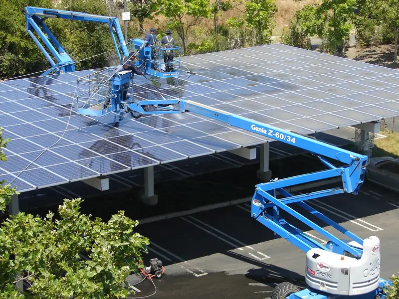 Técnicos limpiando una hilera de paneles solares desde una grúa de canastilla