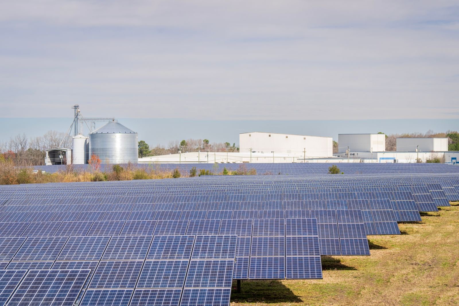 Campo de paneles solares junto a naves industriales y silos