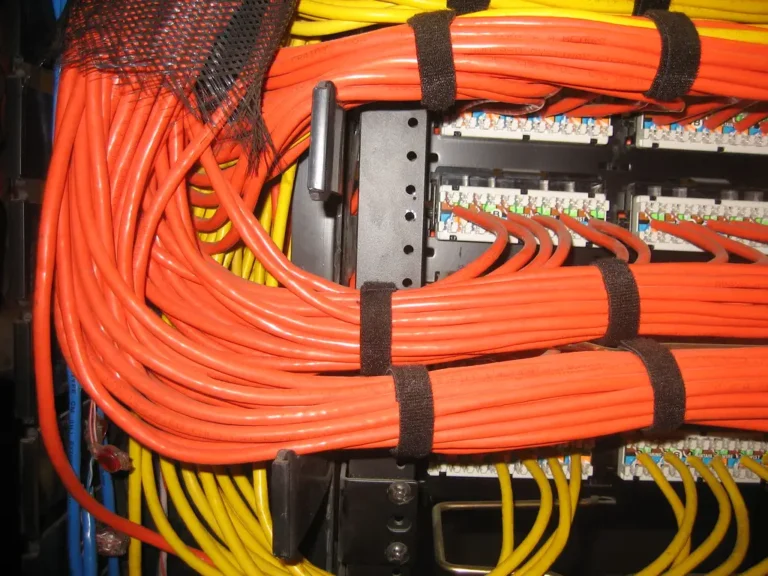 Patch panel de un rack con cables de red naranjas y amarillos ordenados y sujetos con velcro