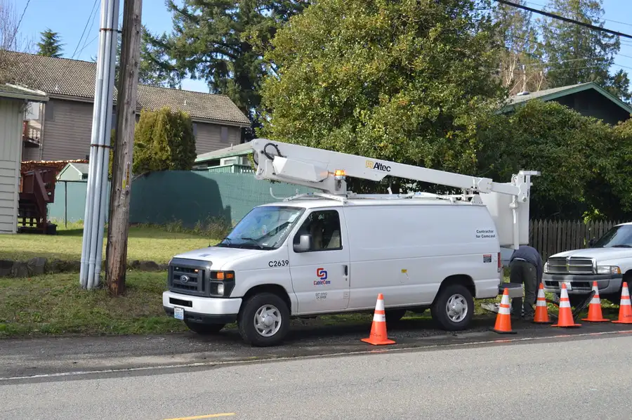 Camioneta con canastilla instalando fibra óptica en postes de una calle