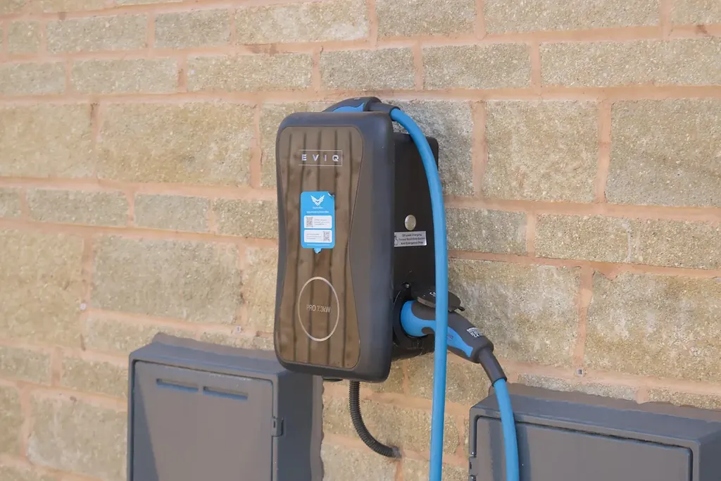 Cargador de pared para autos eléctricos con su cable, instalado sobre un muro de block