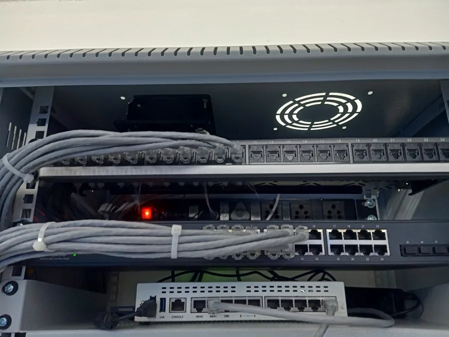Interior de un gabinete de red con ventilador en el techo, patch panel, switch y router