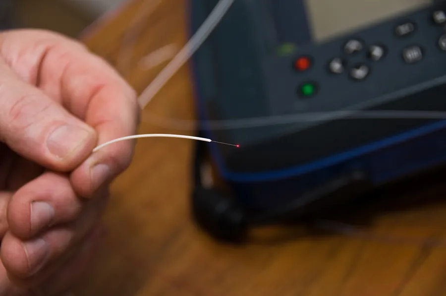 Mano sosteniendo un hilo de fibra óptica pelado, más delgado que un cabello