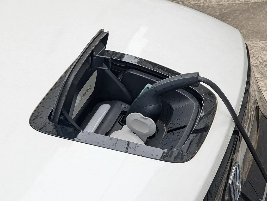 Puerto de carga abierto en el cofre de un auto, con el conector puesto