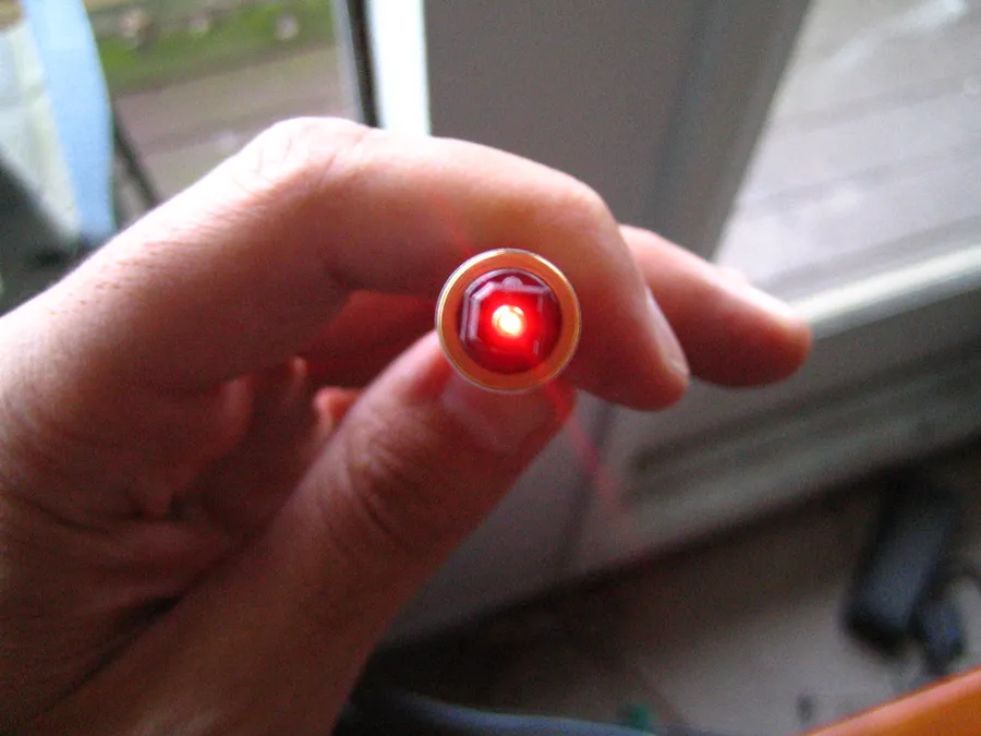 Punta de un cable de fibra óptica encendida con luz roja entre los dedos