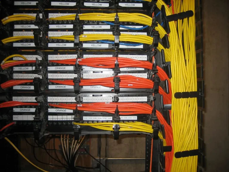 Rack de red con patch panels y organizadores, cables amarillos y naranjas etiquetados por color