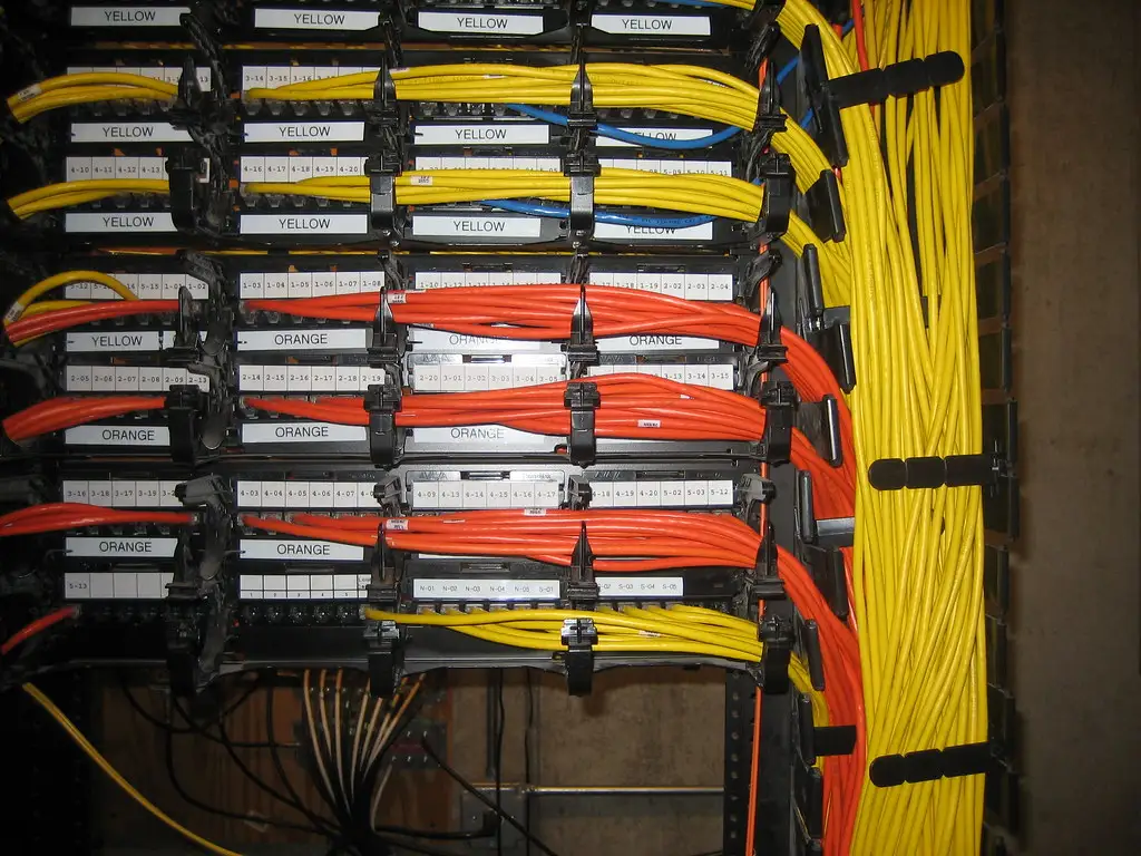 Rack de red con patch panels y organizadores, cables amarillos y naranjas etiquetados por color