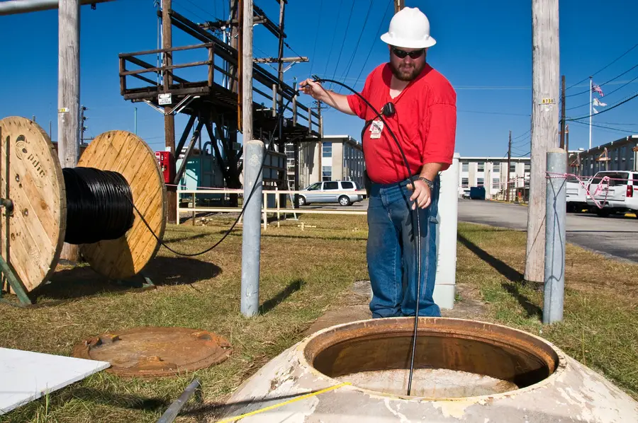 Técnico jalando cable de fibra óptica desde un carrete hacia un registro subterráneo
